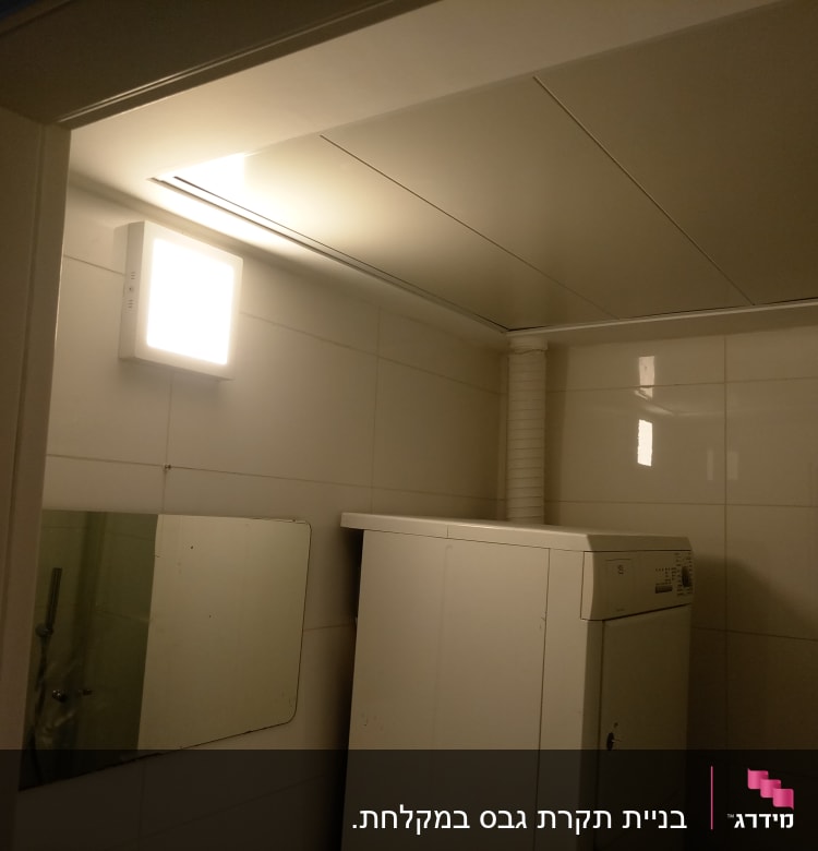 מכונת כביסה בחדר עם קירות גבס ותאורה עליונה